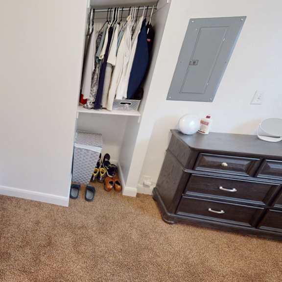 a room with a carpeted floor and a closet with clothes hanging.