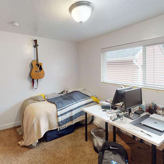 a room with a bed, desk, and a guitar hanging on the wall.
