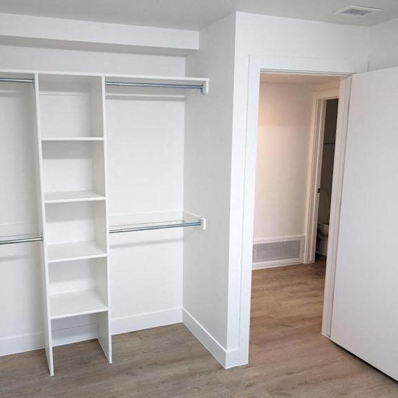 a walk in closet with white shelves and a mirrored closet door