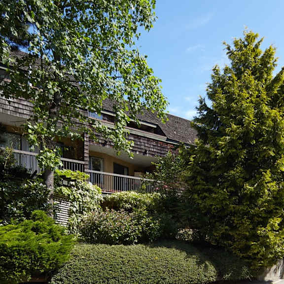 a building with a gray roof and green bushes and trees in front of it