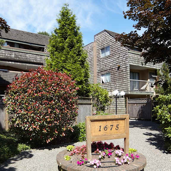 a yard with a sign and flowers in front of an apartment building