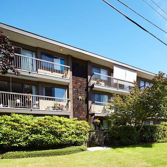 a picture of an apartment building with a green lawn and trees in front of it