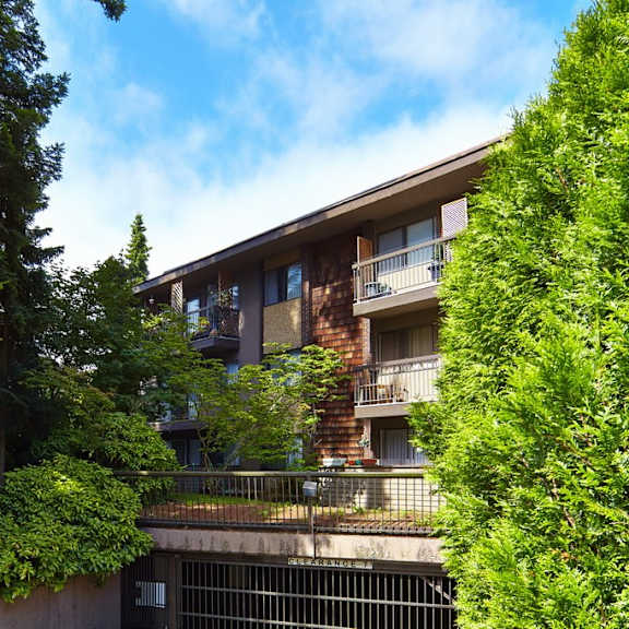 a picture of an apartment building with trees in the foreground and a blue sky in the background