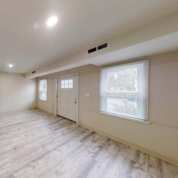 a spacious room with wooden flooring and white walls.