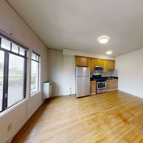 a large empty room with wooden floors and a kitchen area in the background.