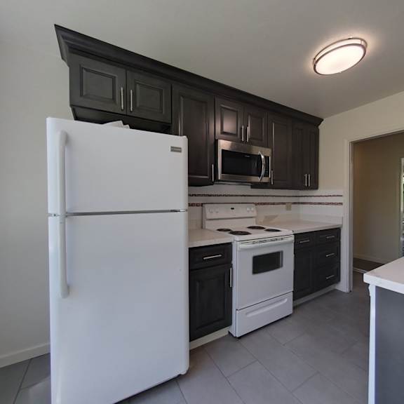 a white refrigerator stands in a kitchen with black cabinets.