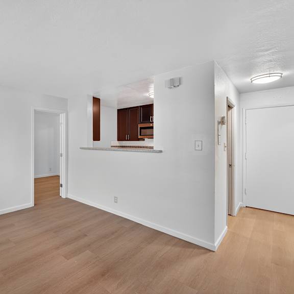 a room with white walls and wooden flooring, with a doorway leading to another room.