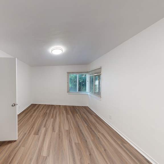 a room with wooden flooring and a window with blinds.