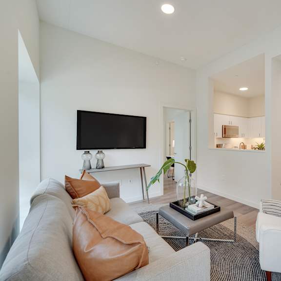 a living room with a grey couch, a white chair, and a television on the wall.