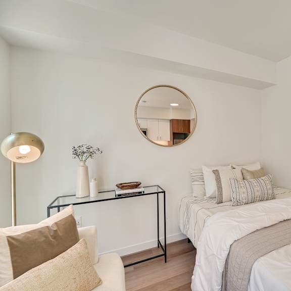 a bedroom with a bed, a table with a vase, and a round mirror on the wall.
