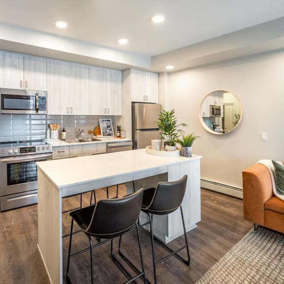 A modern kitchen with a white island and black chairs.