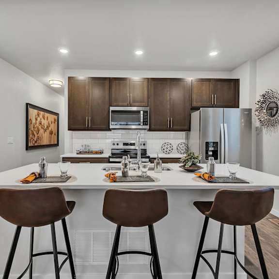 a modern kitchen with white countertops and brown bar stools.