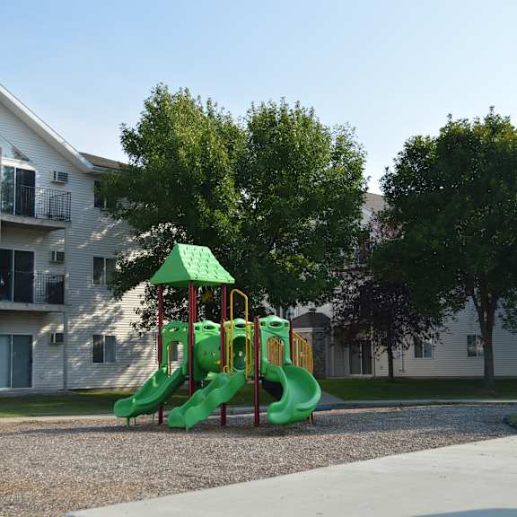 a playground with a green slide in front of apartment buildings.