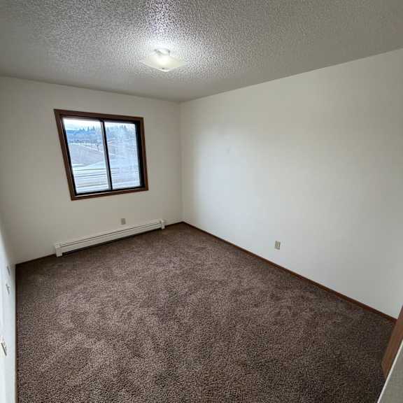 a small window in a white room with a brown carpet.