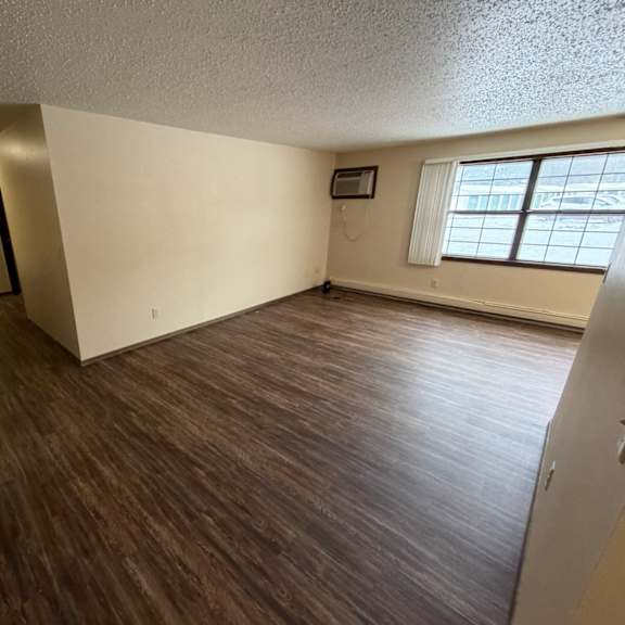 a room with wooden flooring and a window with white curtains.