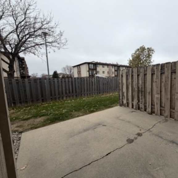 a wooden fence separates a driveway from a grassy area.