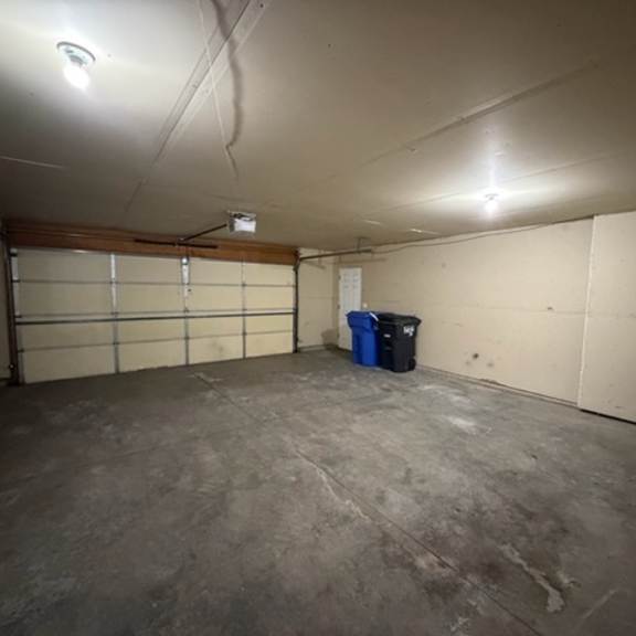 a blue bin sits in the corner of a concrete garage.