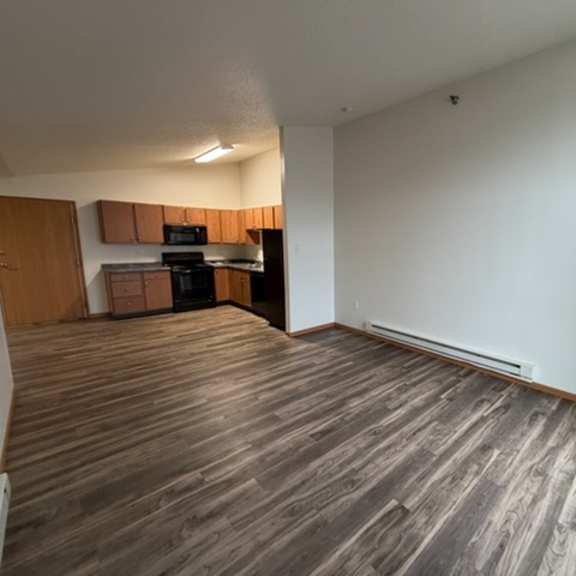 a room with wooden flooring and a kitchen area in the background.