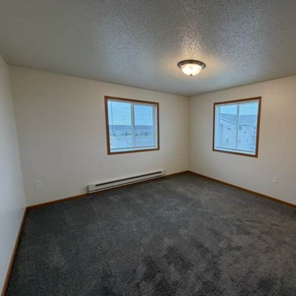 a room with a grey carpet and two windows.