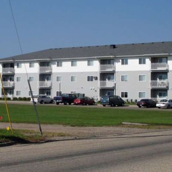 a large white apartment building with a parking lot in front.