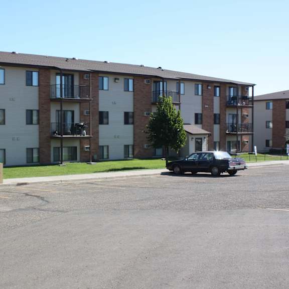 a black car is parked in a parking lot in front of apartment buildings.