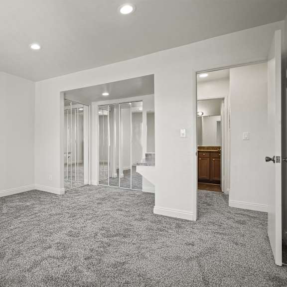 a spacious room with a carpeted floor and a staircase with glass doors.