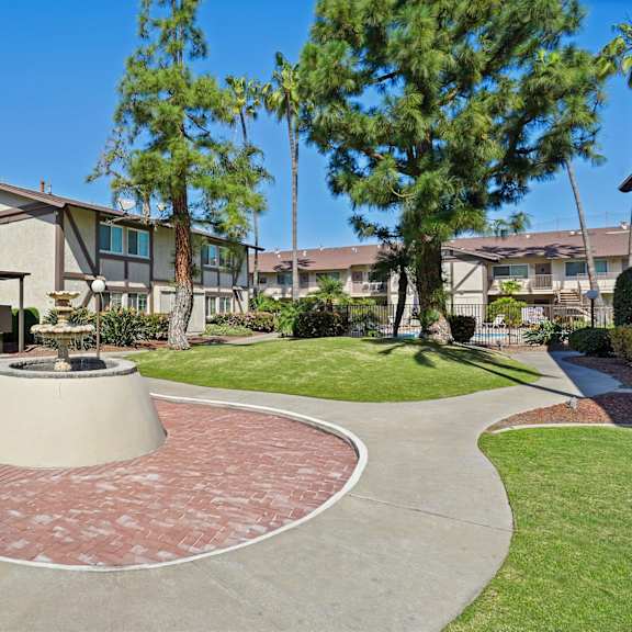 a courtyard with a fountain surrounded by houses and trees.
