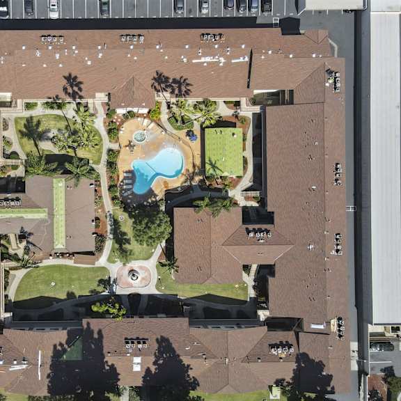 an aerial view of a parking lot, a building, and a green space with a fountain.