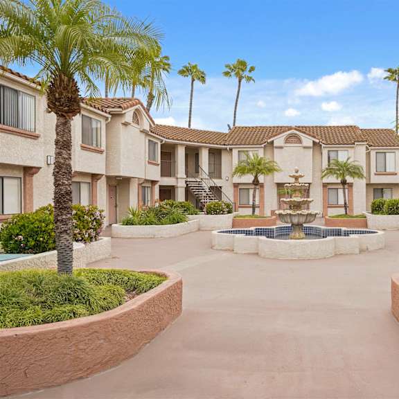 a courtyard with palm trees and a fountain in the middle of apartment buildings.