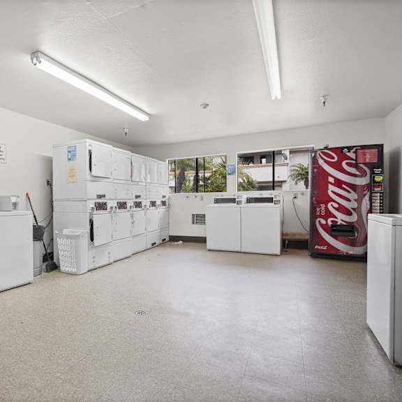 a coca cola vending machine sits in a white room with a washing machine and dryer.