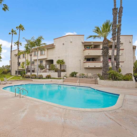 a swimming pool surrounded by palm trees and lounge chairs in front of a building.