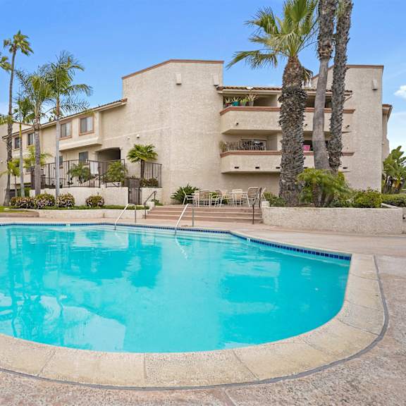 a swimming pool in front of a building with palm trees.