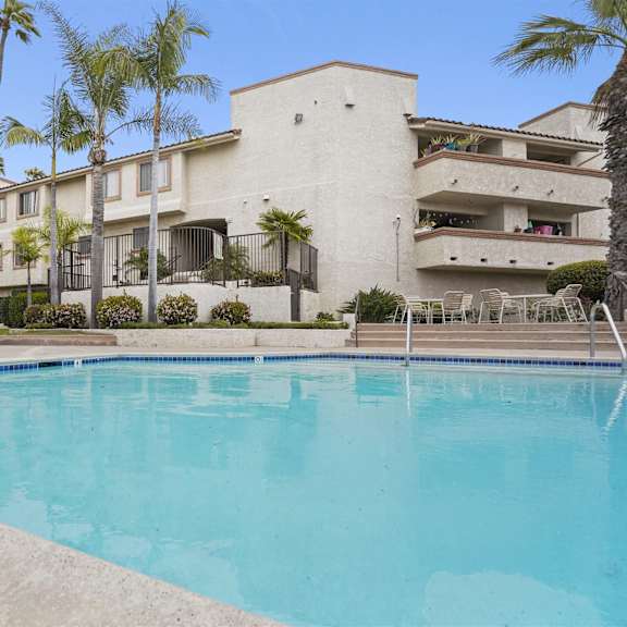 a swimming pool in front of a building with palm trees.