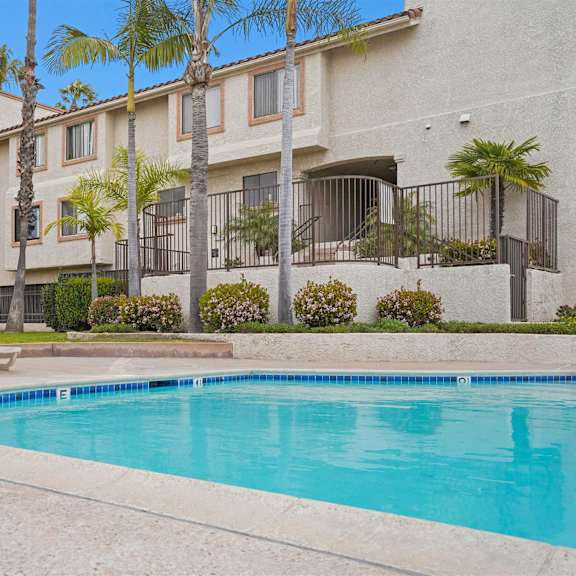 a swimming pool in front of a building with palm trees.
