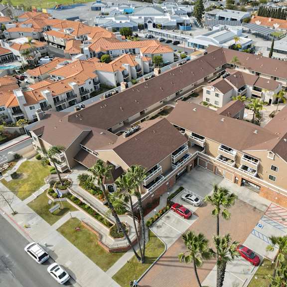 a large building with a brown roof is surrounded by smaller buildings and palm trees.