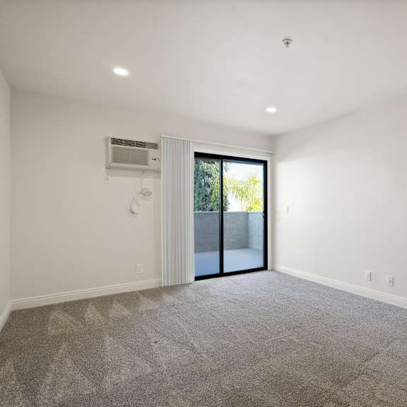 a spacious room with a carpeted floor and a sliding glass door leading outside.