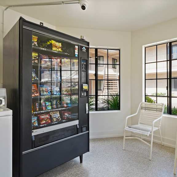a black vending machine sits in a room with two white chairs.