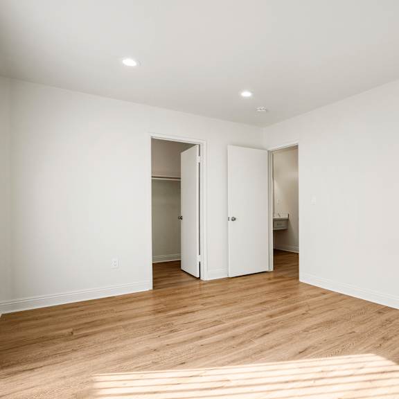a room with white walls and wooden flooring with a doorway open to another room.