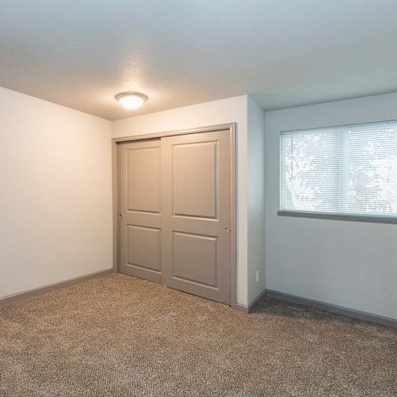 a room with a carpeted floor, a white door, and a window with blinds.