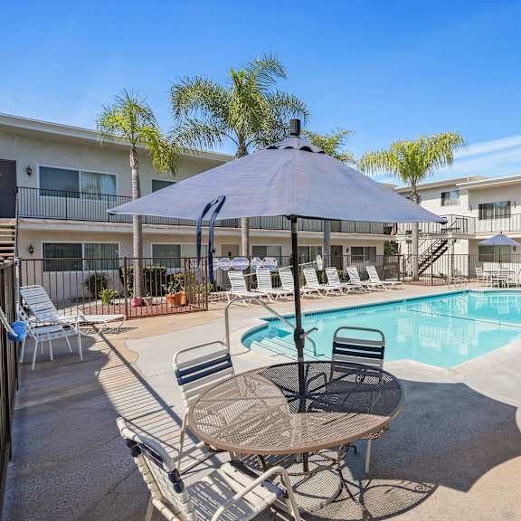a pool area with a table and chairs and a pool in the middle.