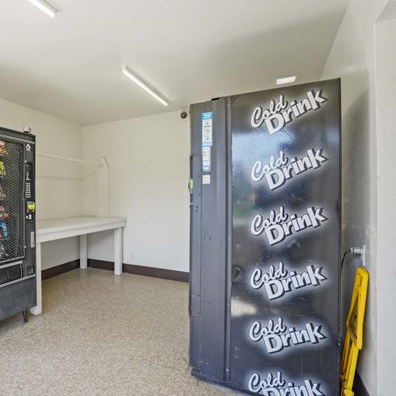 a black coca-cola fridge sits in a room with a bench.