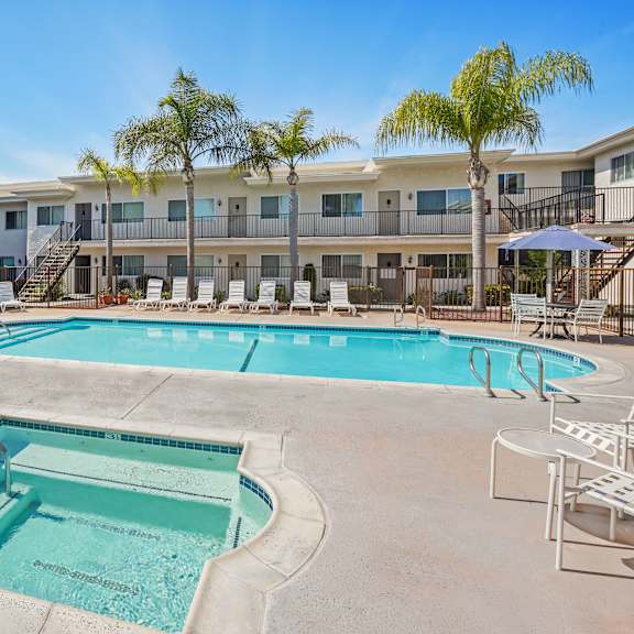 a swimming pool surrounded by lounge chairs and umbrellas in front of a building with palm trees.