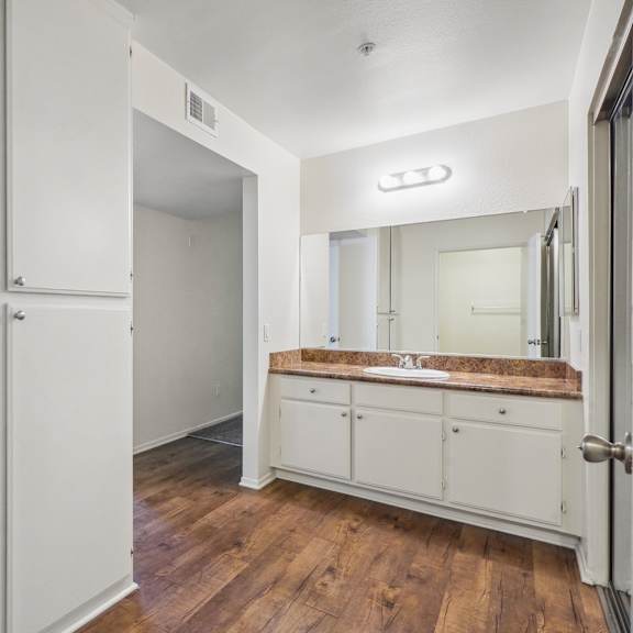 a white bathroom with a wooden floor and a mirror above the sink.