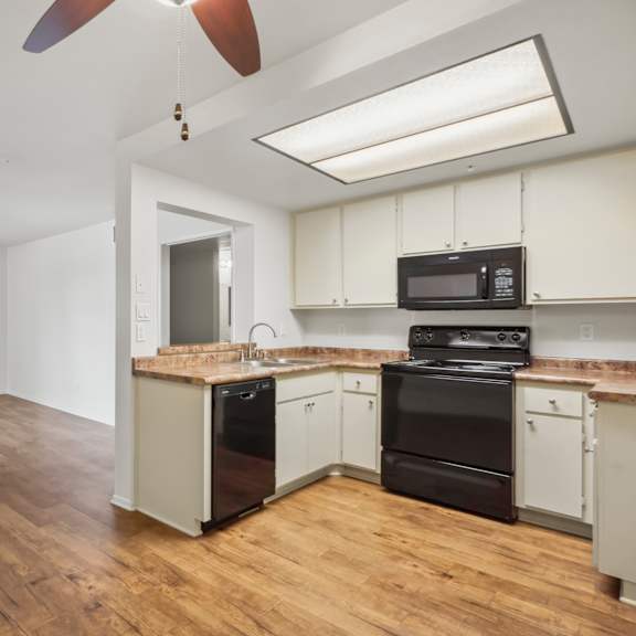 a kitchen with black appliances and wooden floors.