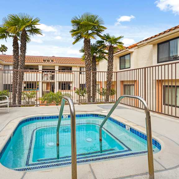 a pool surrounded by palm trees and a building in the background.