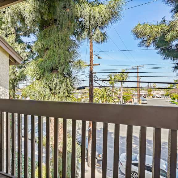 a balcony with a metal railing overlooks a street with cars and trees.