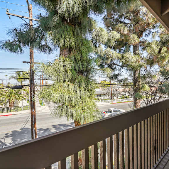 a balcony with a wooden floor and a railing overlooks a street with cars and trees.