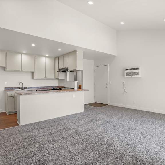 a spacious kitchen with white cabinets and a grey carpet.