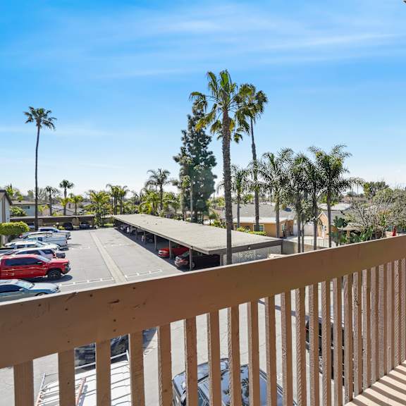 a balcony with a view of a parking lot and palm trees.