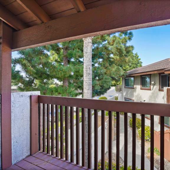 a wooden deck with a railing overlooking a house and trees.